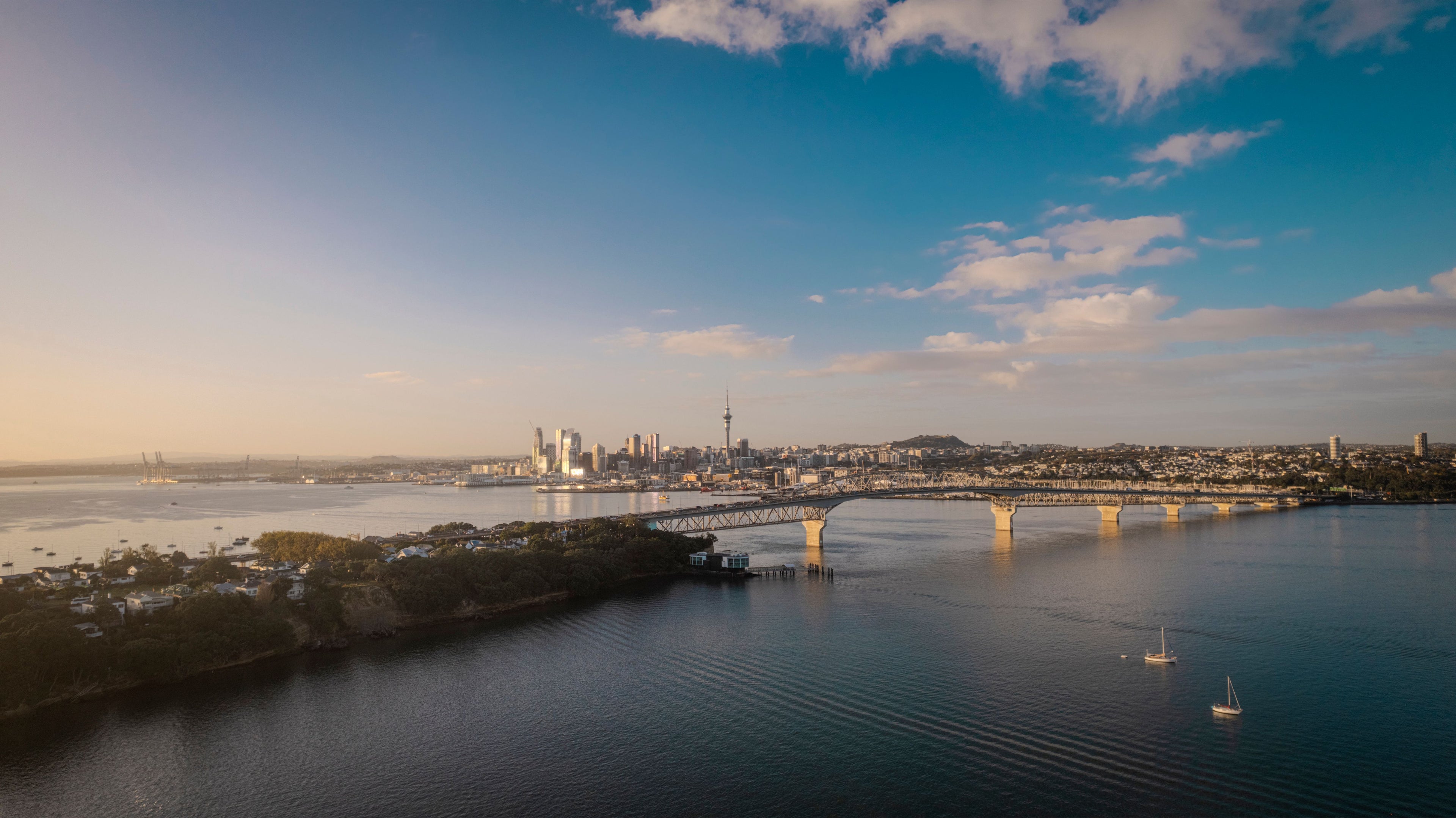 Auckland Cityscape with a harbor bridge over water under a blue sky with clouds