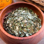 House of Rehua detox tea leaves in a round wooden bowl, with a glass pitcher and wicker basket in the background.