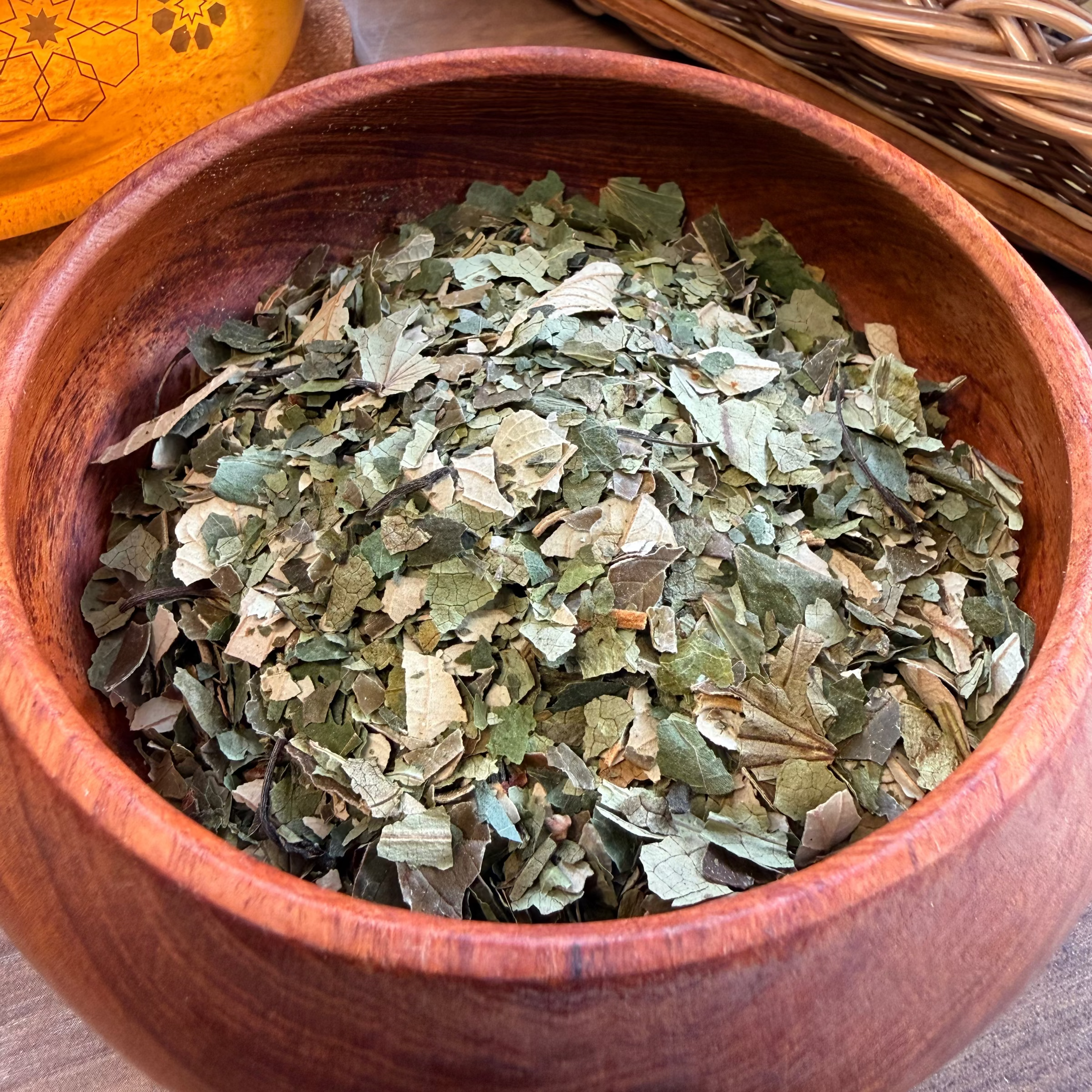 House of Rehua detox tea leaves in a round wooden bowl, with a glass pitcher and wicker basket in the background.