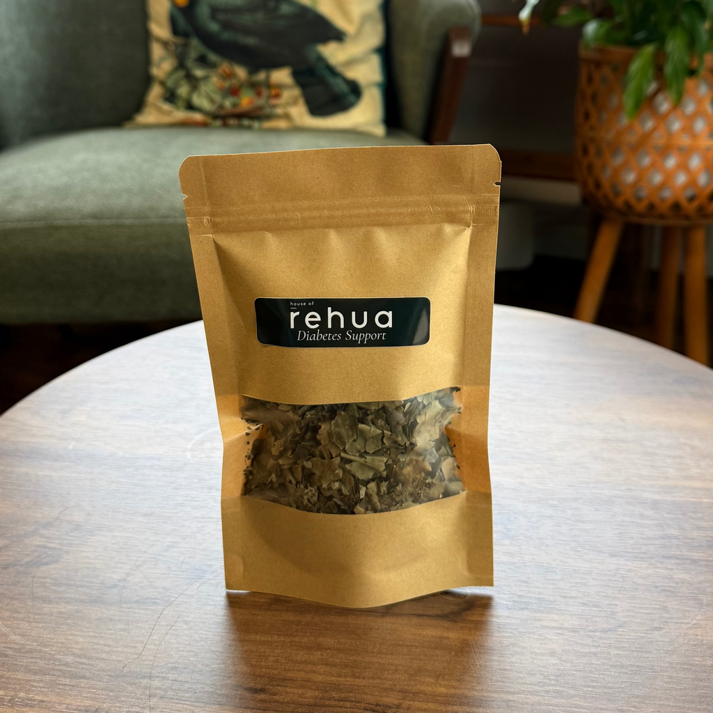 A stand-up pouch of House of Rehua Diabetes support tea on a round wooden table in a cozy, plant-filled room with a green armchair and decorative items in the background.