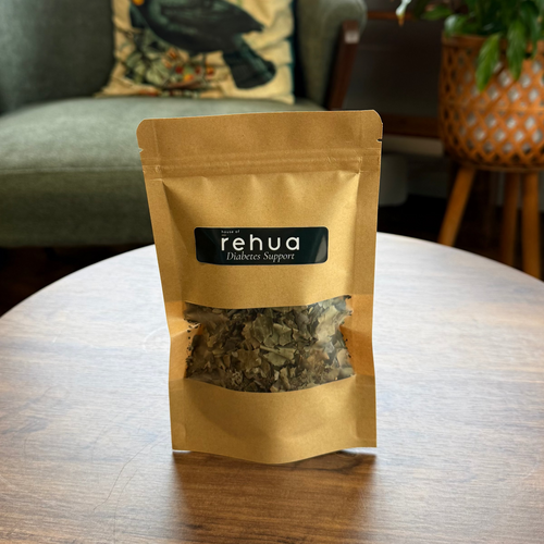 A stand-up pouch of House of Rehua Diabetes support tea on a round wooden table in a cozy, plant-filled room with a green armchair and decorative items in the background.