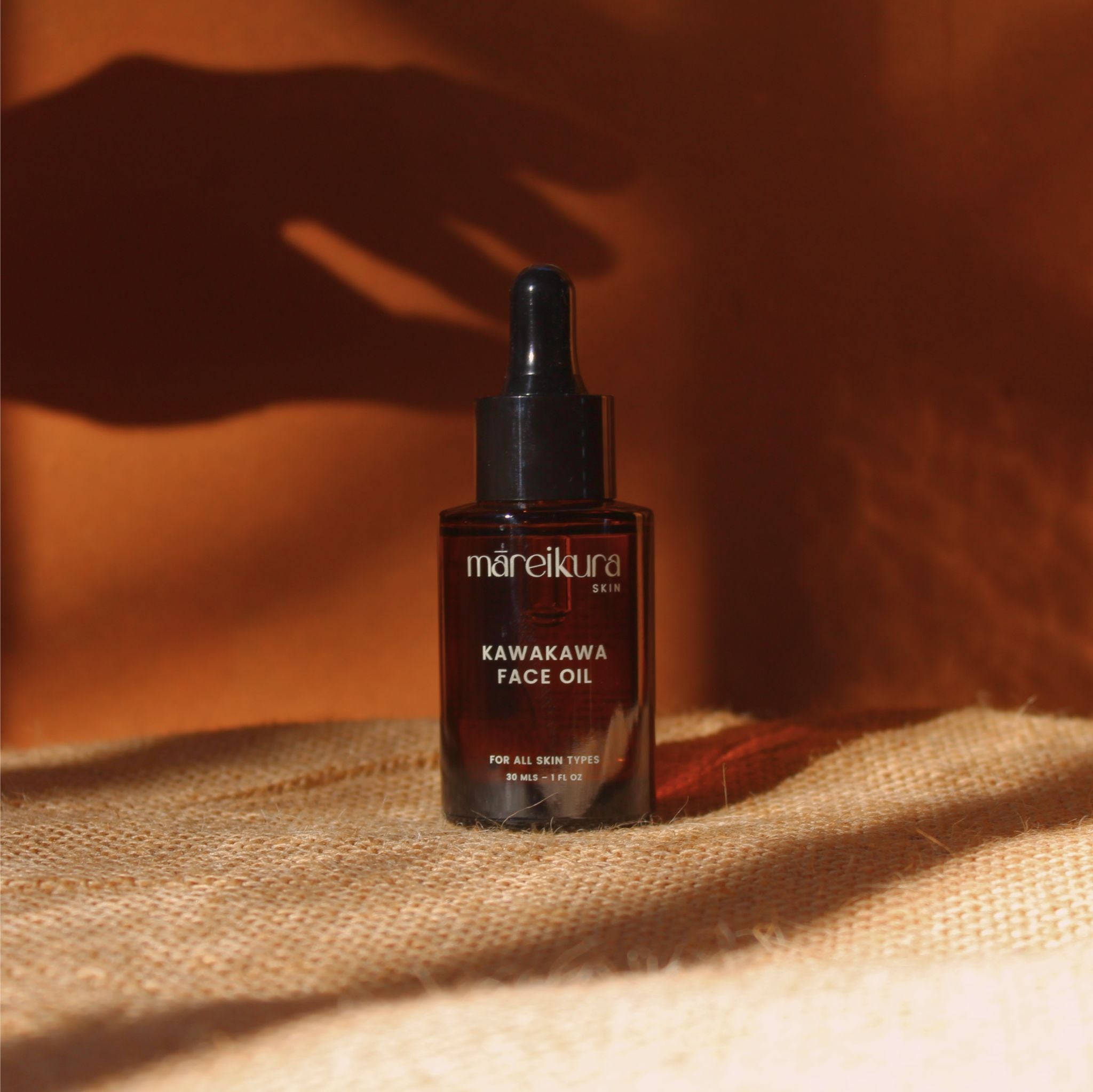 Kawakawa face oil bottle on a textured surface with a warm brown background