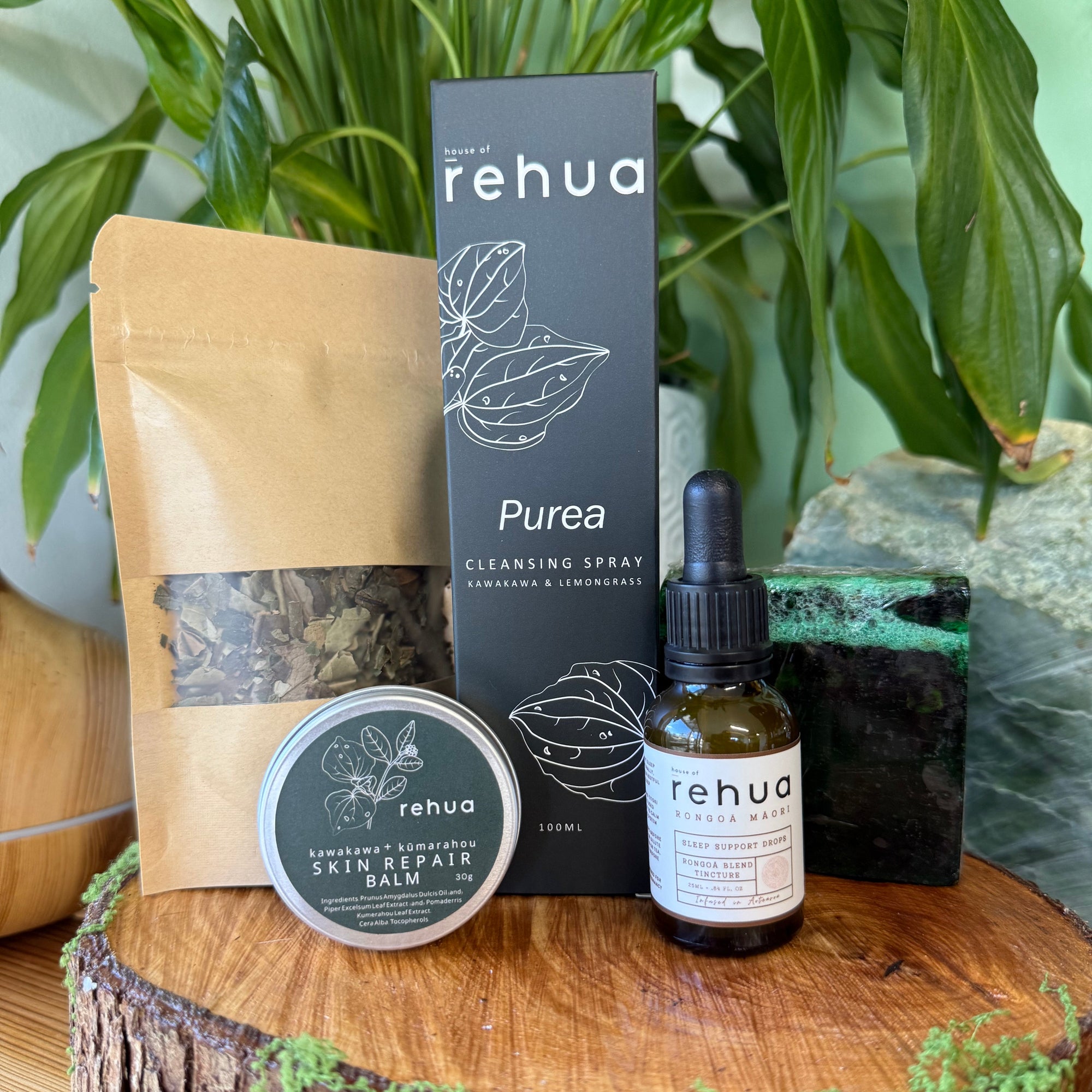 Rehua reset ritual skincare products including a bottle, box, and jar on a wooden surface with plants in the background.