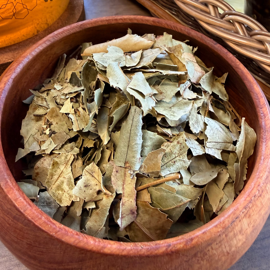 House of rehua Sleep tea leaves piled in a round wooden bowl, with a glass teapot and ceramic cups in the softly blurred background.