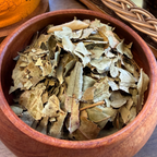 House of rehua Sleep tea leaves piled in a round wooden bowl, with a glass teapot and ceramic cups in the softly blurred background.