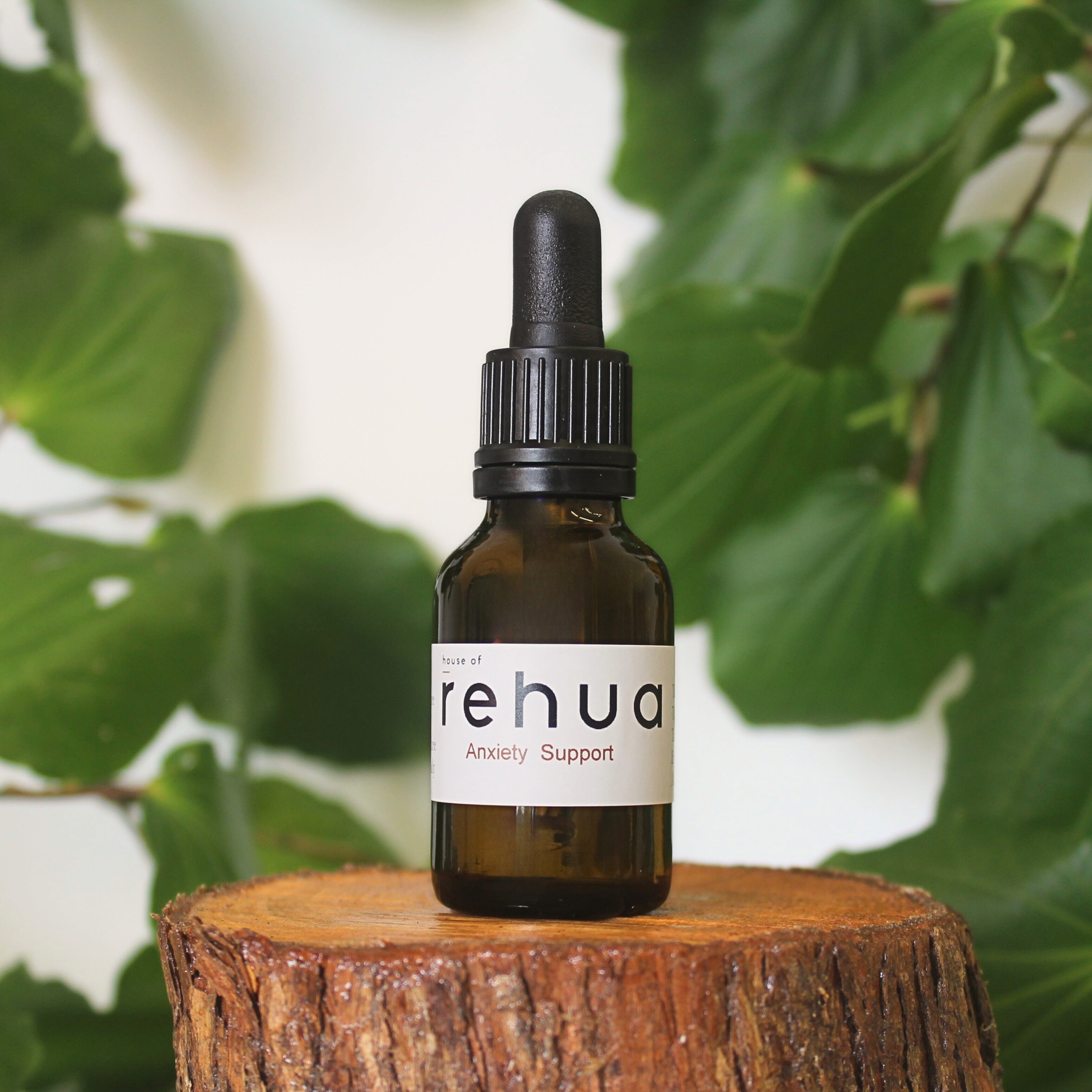 Bottle of House of Rehua Anxiety Support Tincture on a wooden stump with kawakawa leaves in the background