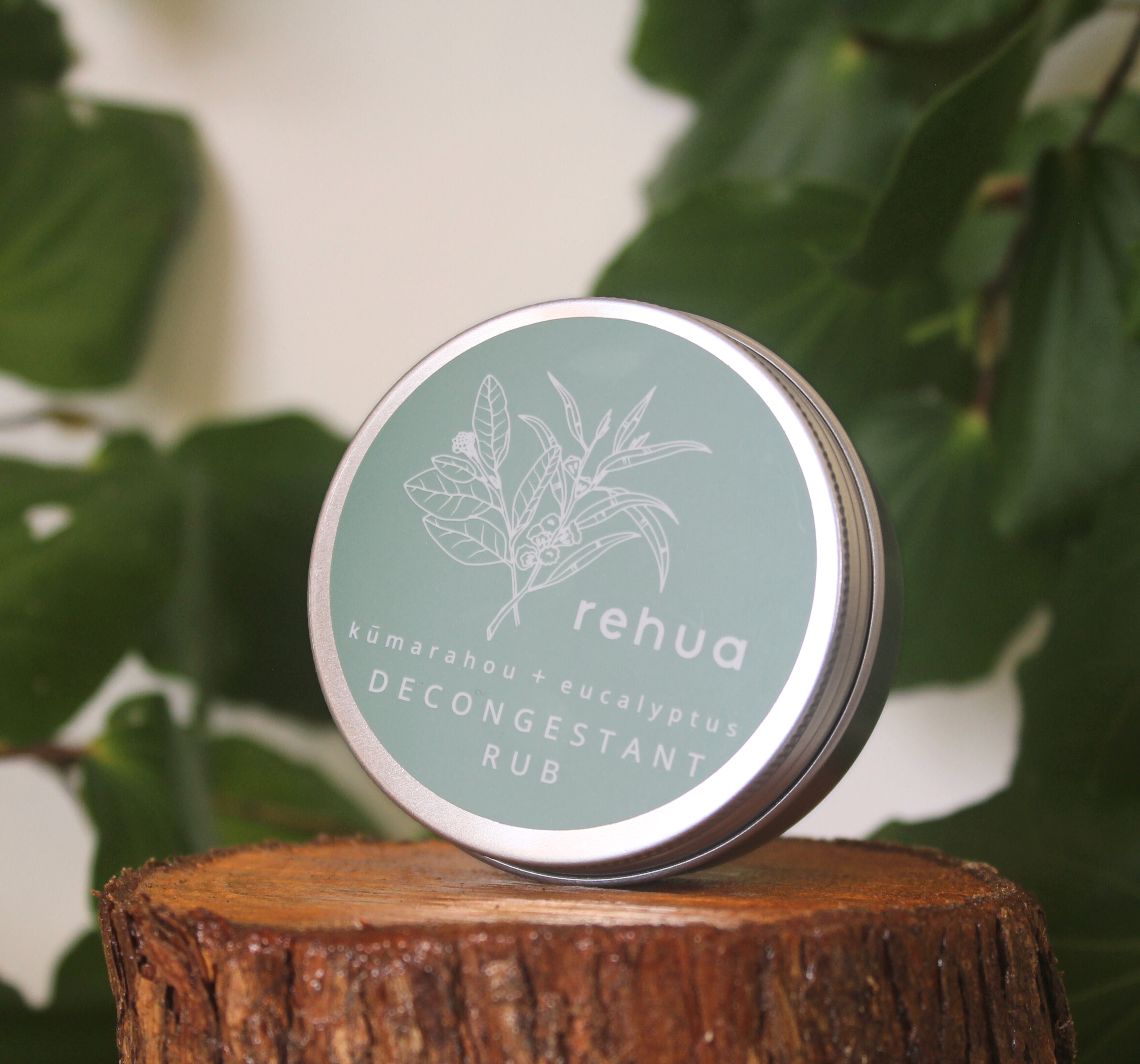 House of Rehua decongestant rub tin on a wooden block with kawakawa leaves in the background