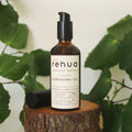 Brown bottle of House of Rehua Kawakawa Body Oil on a wooden stump with kawakawa leaves in the background