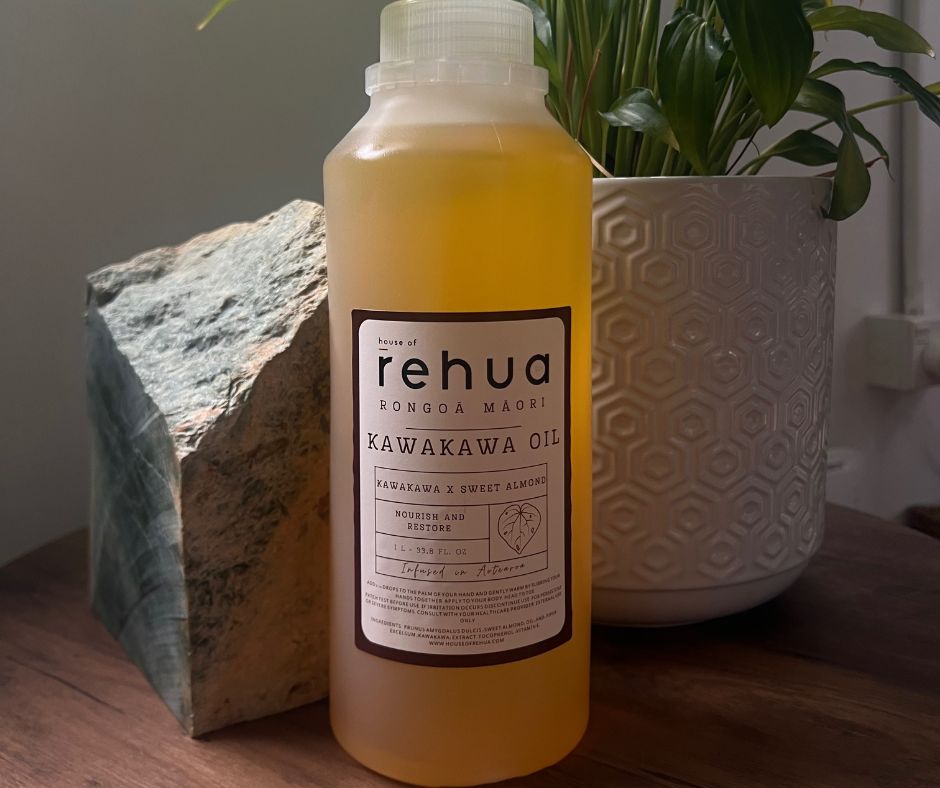 Bottle of rehua Kawakawa Oil on a wooden surface with a plant and rock in the background