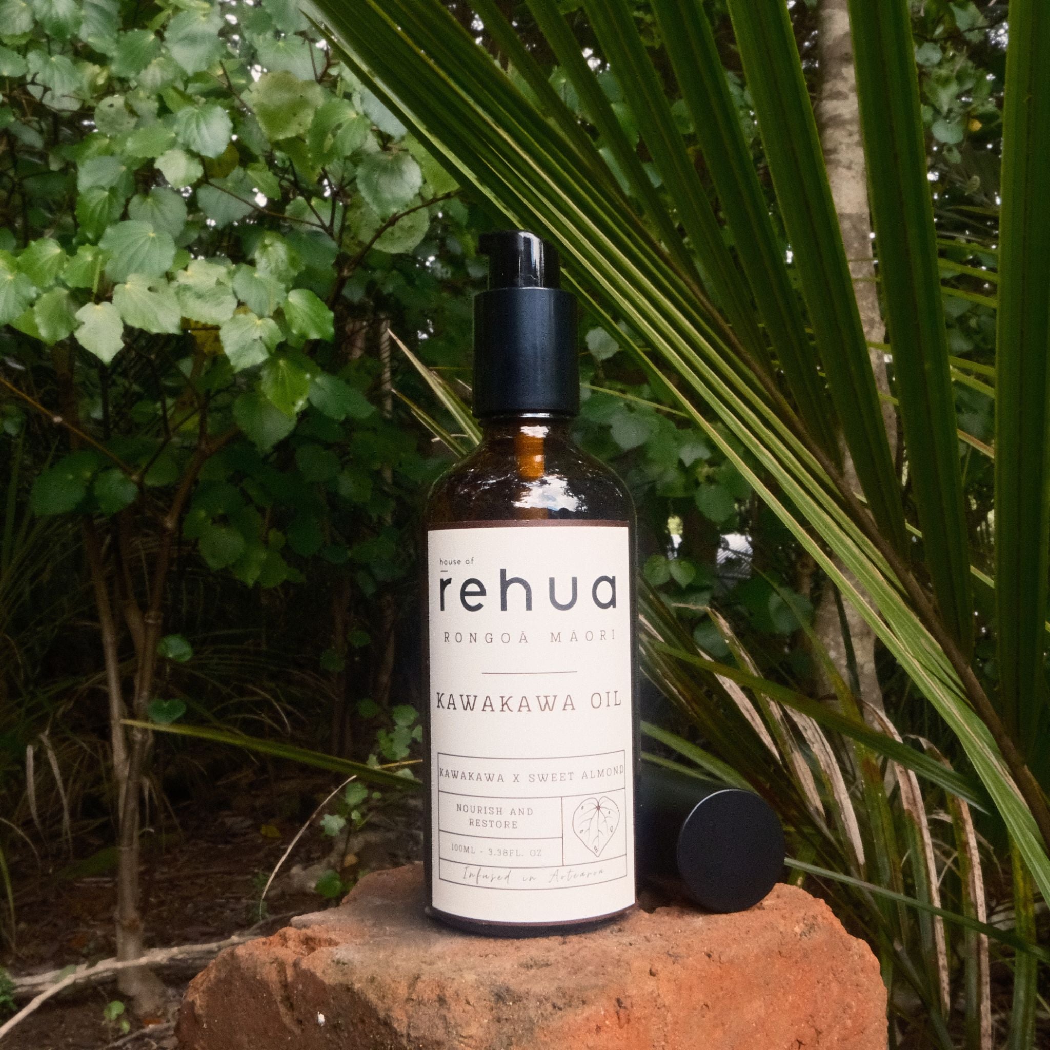 Bottle of House of Rehua kawakawa Oil on a rock with green foliage in the background