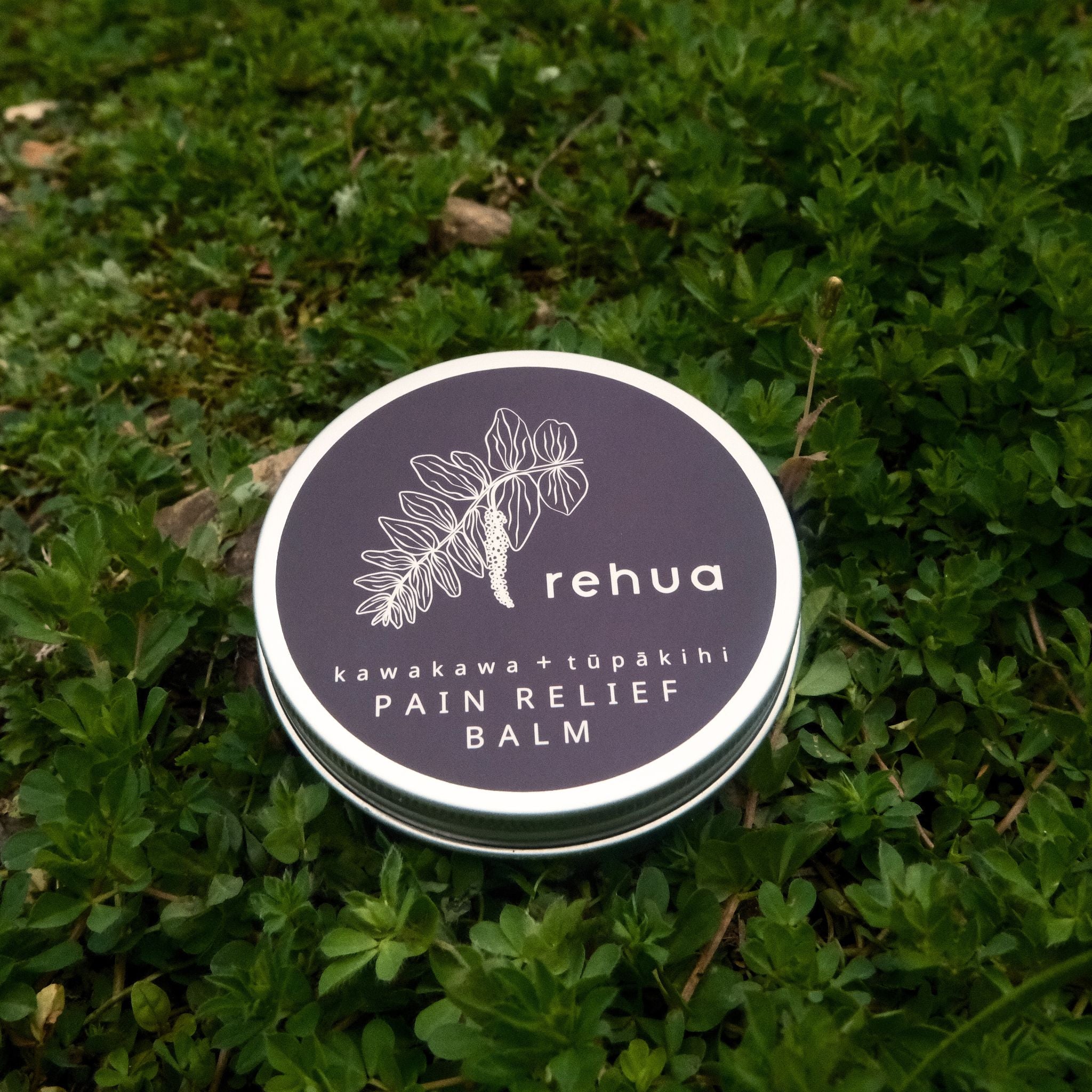 Rehua pain relief balm container on green grass