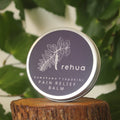 House of Rehua pain relief balm tin on a wooden stump with kawakawa leaves in the background