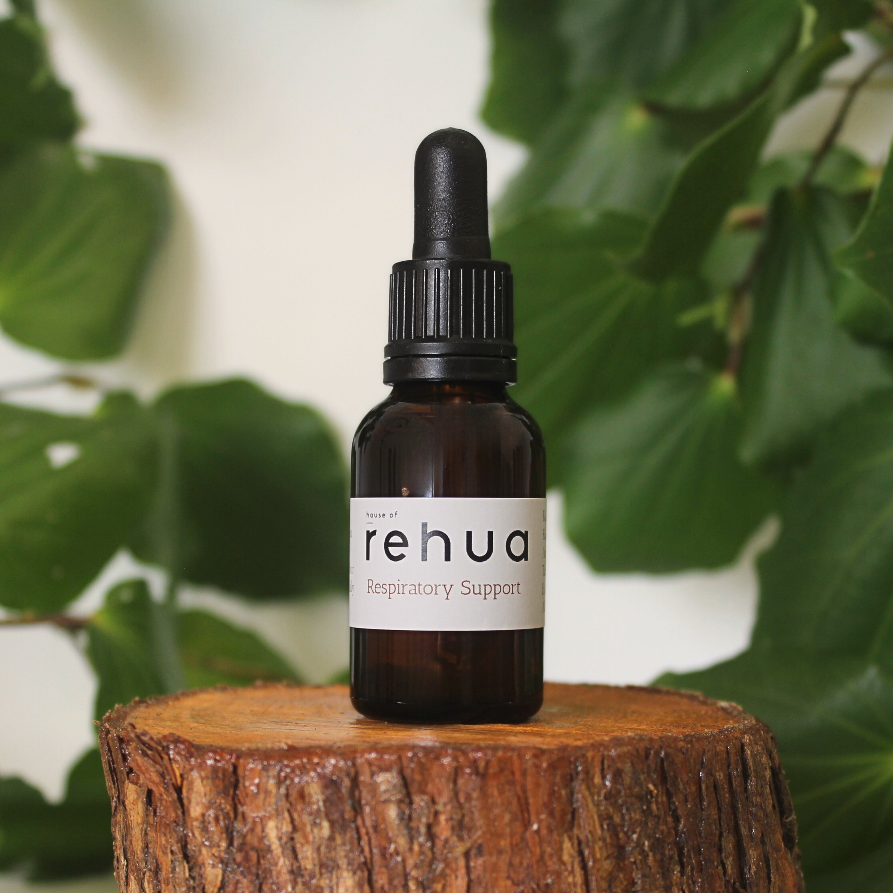 Bottle of House of Rehua Respiratory Support tincture on a wooden stump with kawakawa leaves in the background