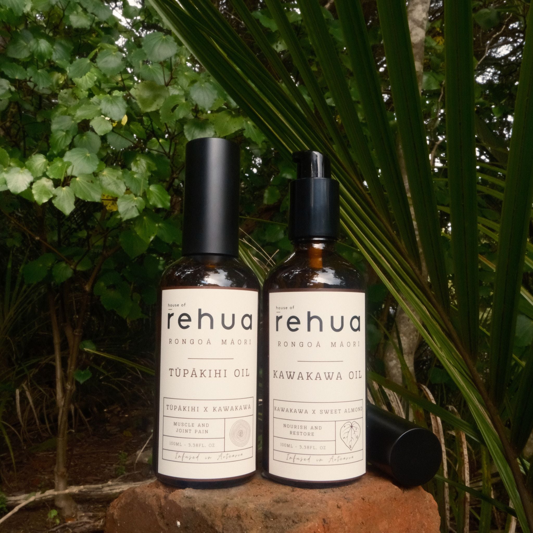 Two bottles of Rehua oils on a rock with green foliage in the background