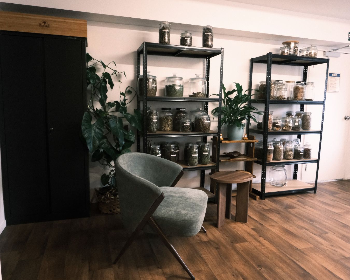 Room with black metal shelves displaying jars, a gray chair, and wooden floor.