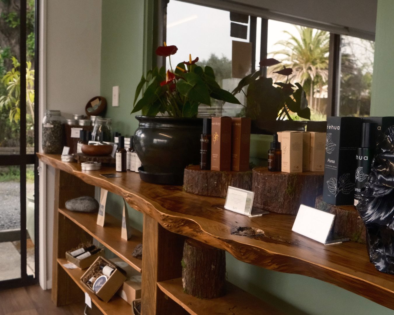 Wooden shelf with various items including plants and boxes in a room with large windows.
