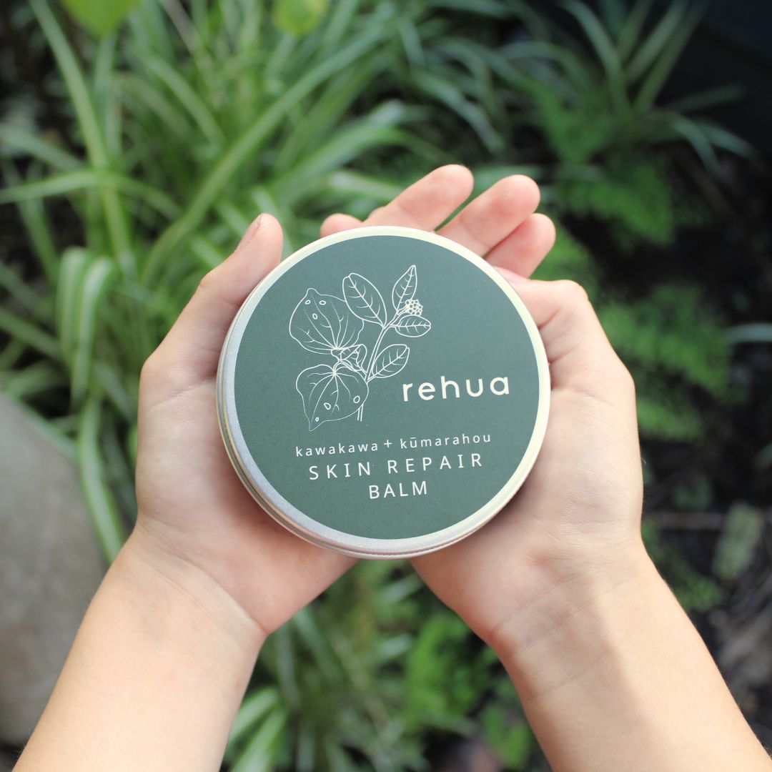 Hands holding a container of rehua skin repair balm with plants in the background