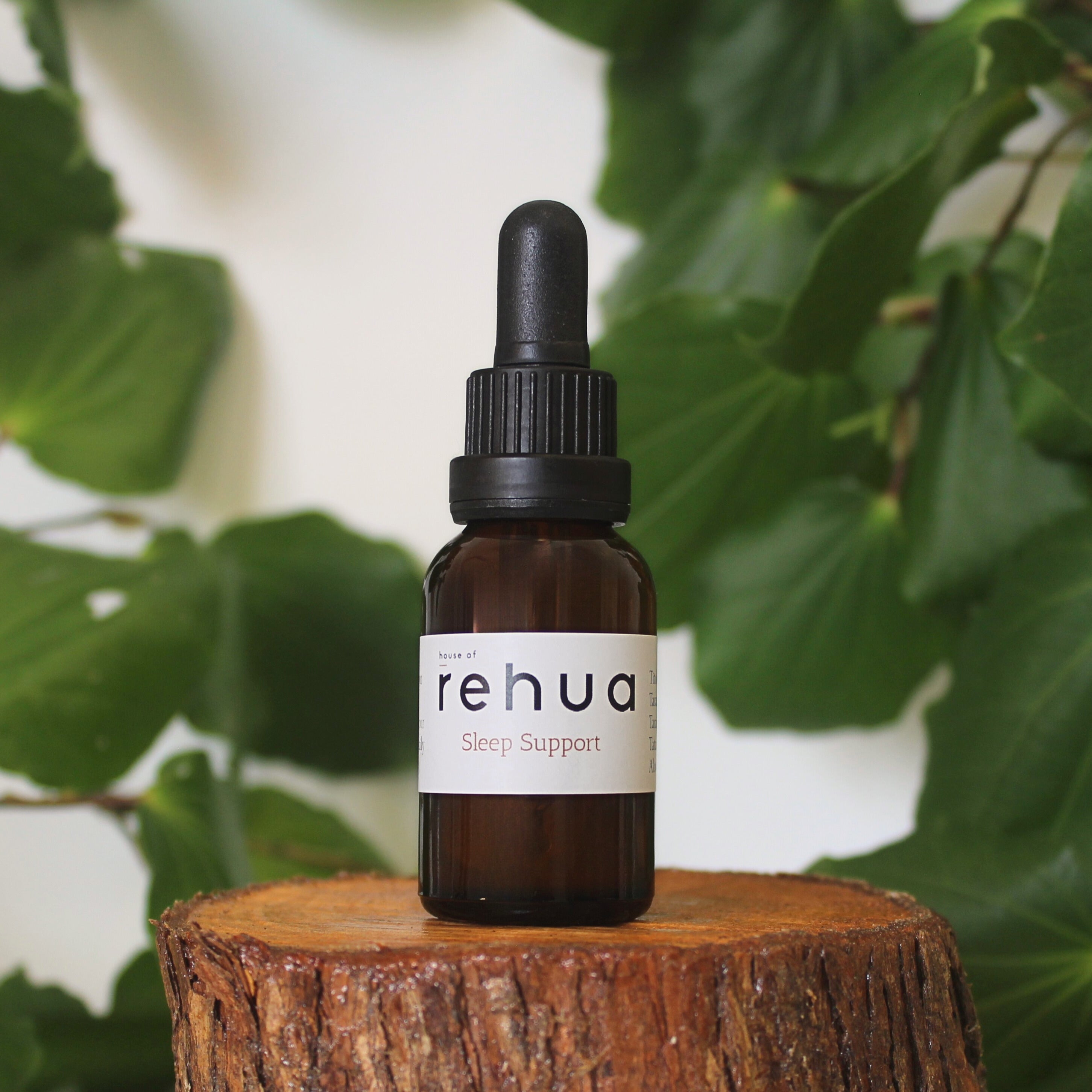 Bottle of House of Rehua Sleep Support Tincture on a wooden stump with kawakawa leaves in the background