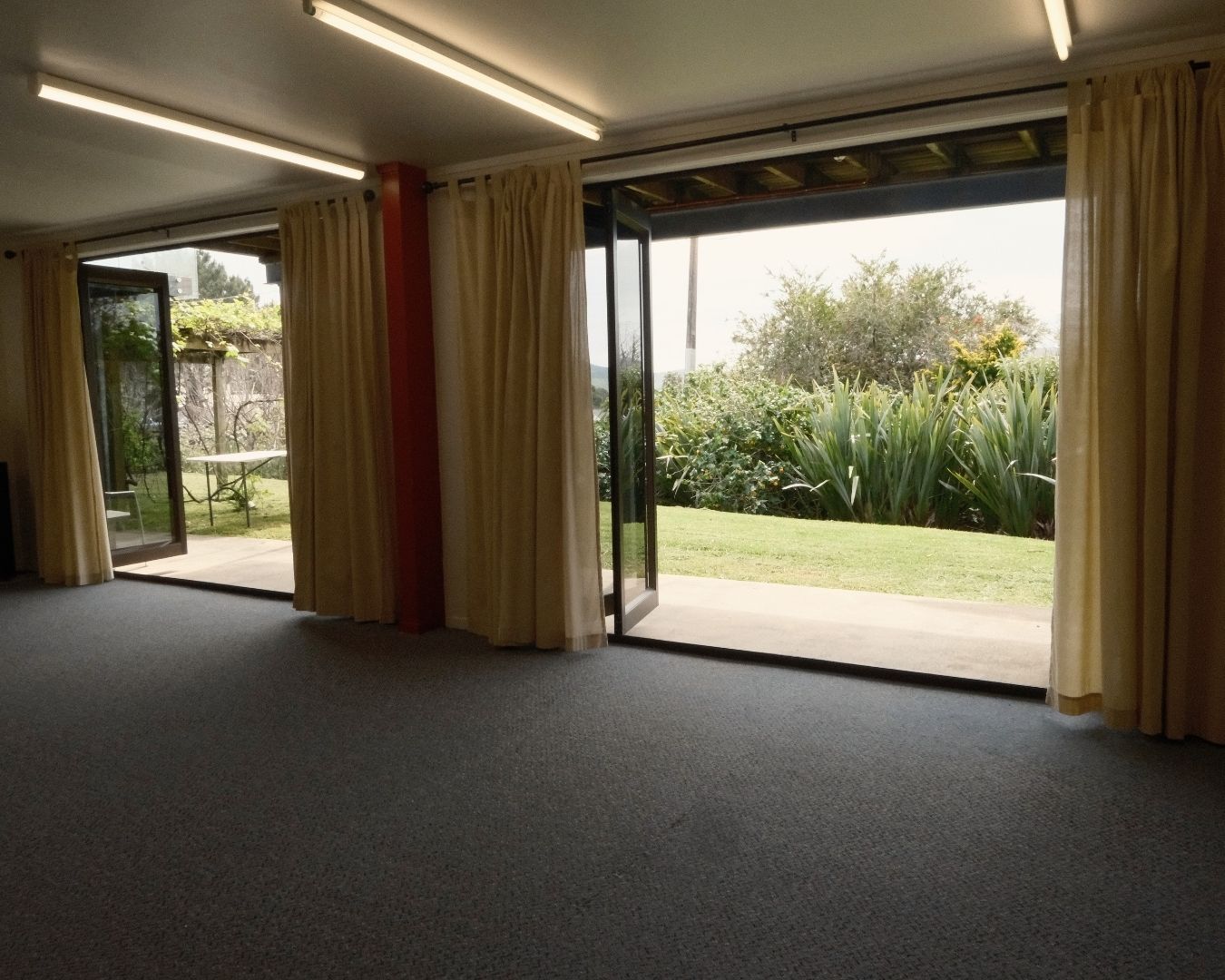 Modern room with large windows and sliding doors, showing a garden view.