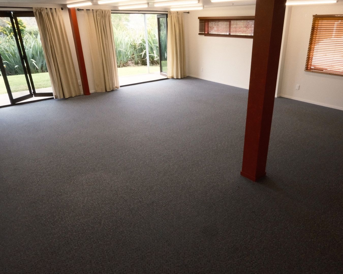Empty room with gray carpet, large windows, and a red column.