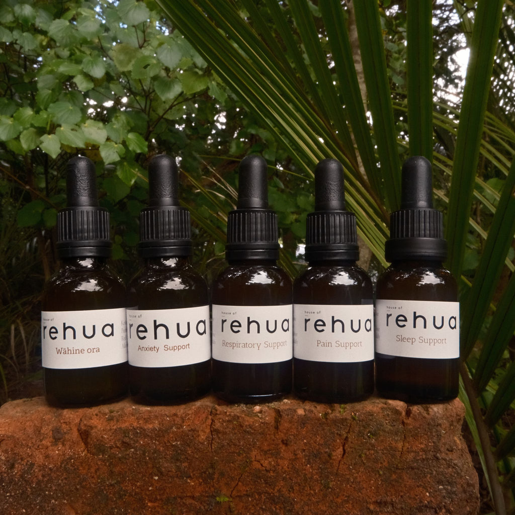 Six bottles of Rehua products on a stone surface with green foliage in the background