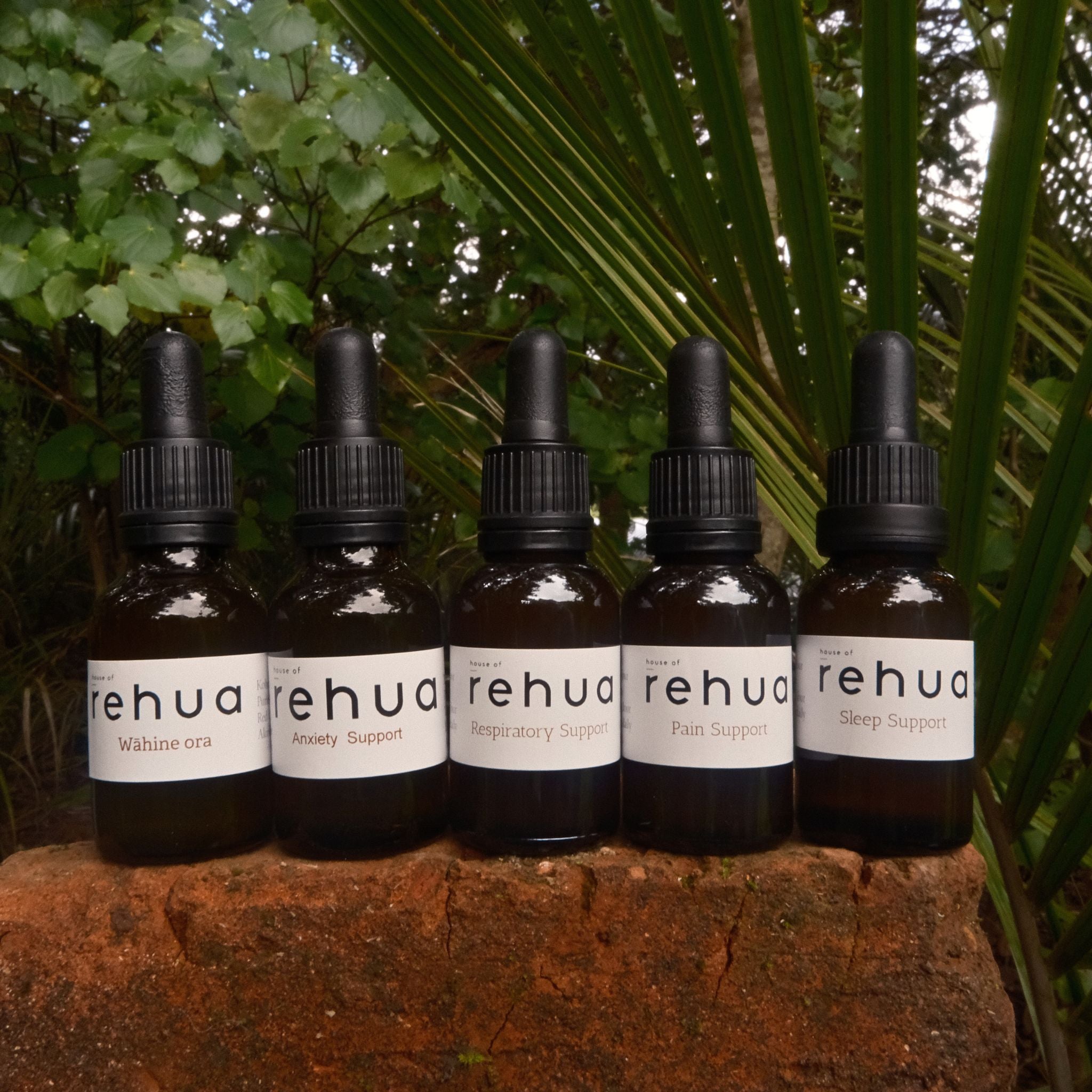 Six bottles of Rehua products on a stone surface with green foliage in the background