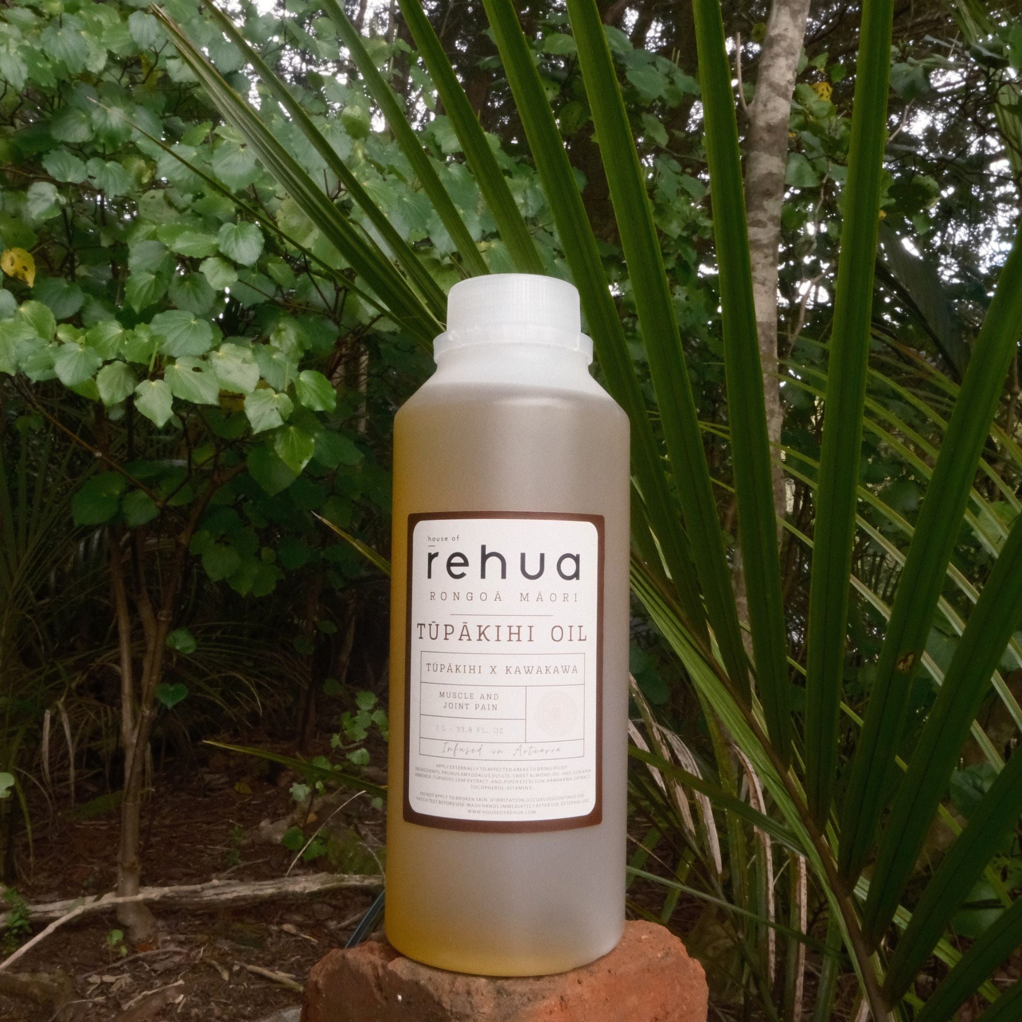 Bottle of rehua Tupakihi oil on a rock with green foliage in the background