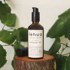 Bottle of House of Rehua Tūpākihi Body Oil on a wooden stump with kawakawa leaves in the background