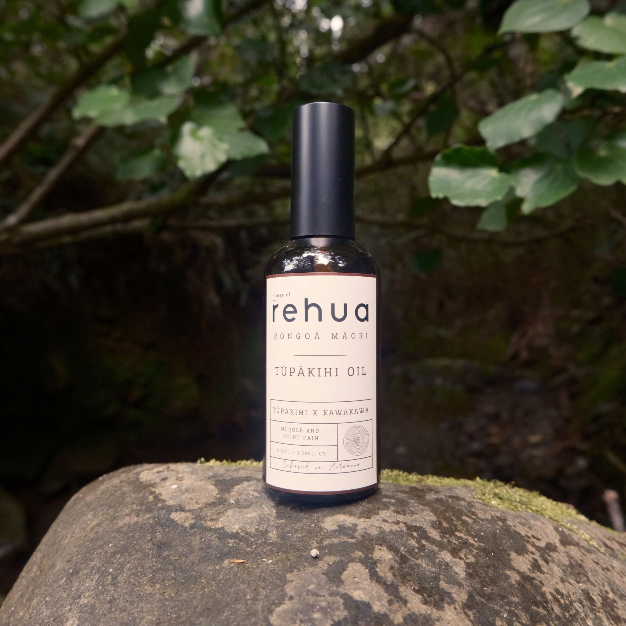 Bottle of Rehua Tupakihi Oil on a rock with greenery in the background