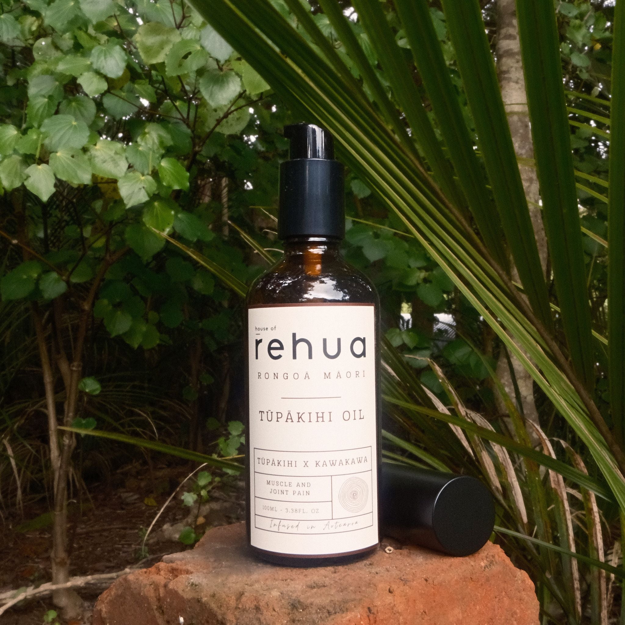 Bottle of House of Rehua Tupakihi Oil on a stone surface with green foliage in the background