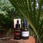 Two bottles of skincare products on a rock with green foliage in the background