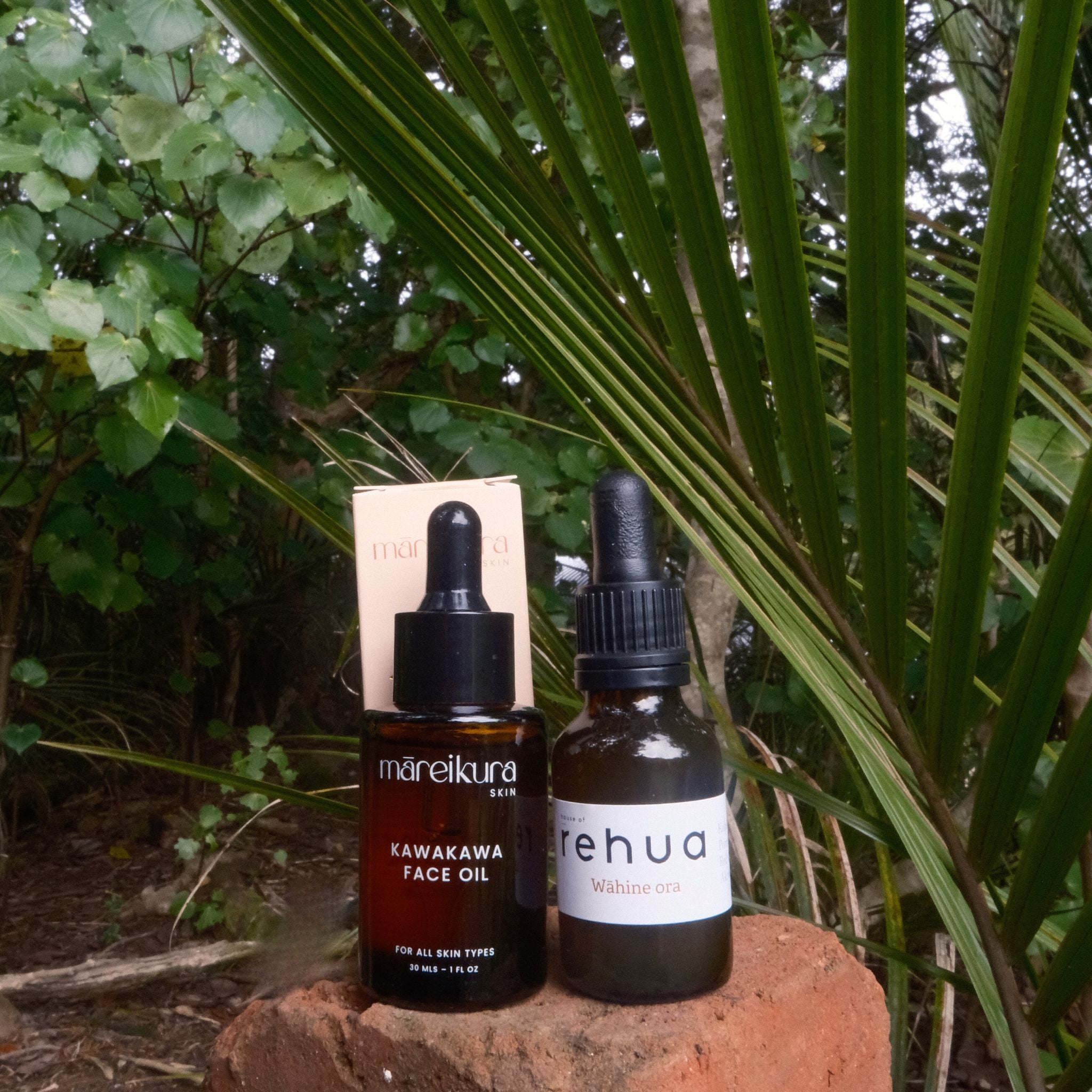 Two bottles of skincare products on a rock with green foliage in the background