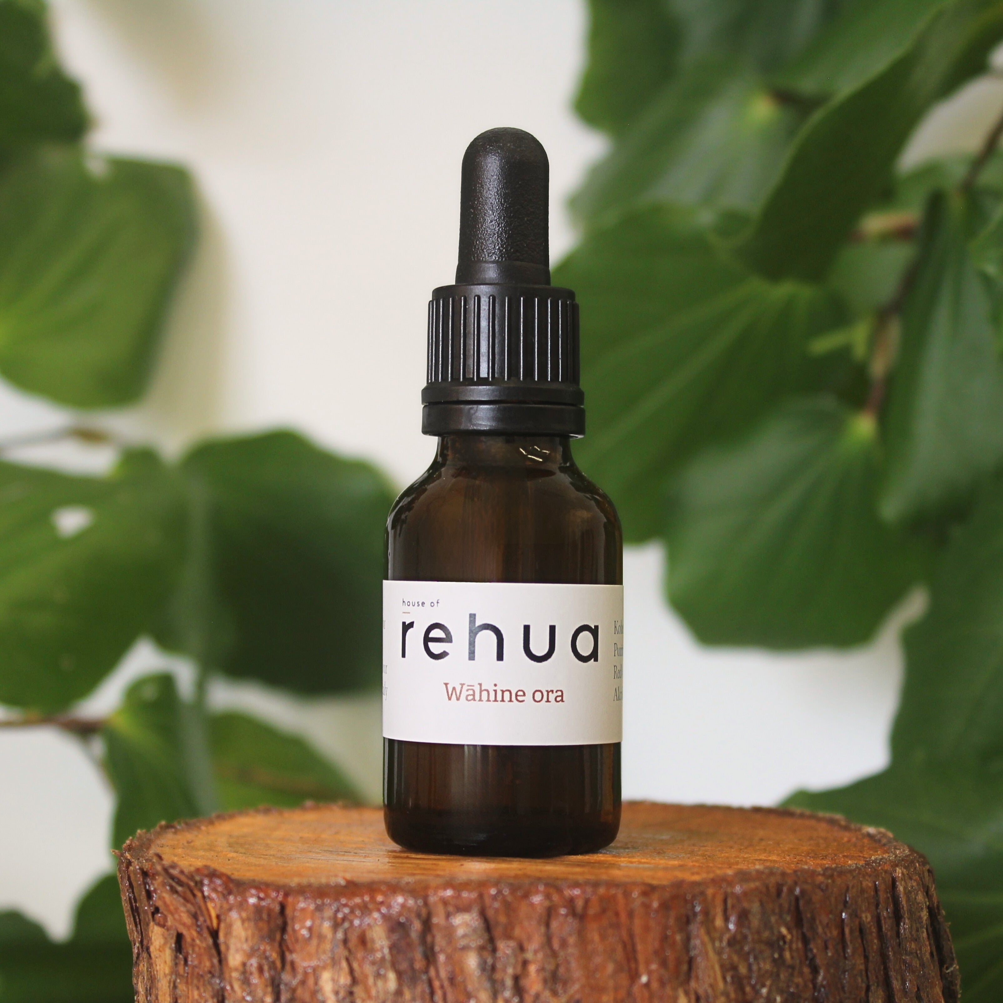 Bottle of House of Rehua Wāhine Ora Tincture on a wooden stump with kawakawa leaves in the background