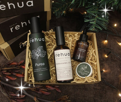Three 'rehu' skincare products in a box with decorative lights and greenery.