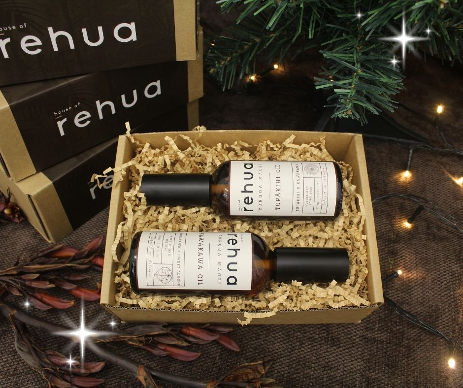 two bottles of Rehua oil in a box with decorative lights and greenery in the background.