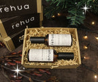 two bottles of Rehua oil in a box with decorative lights and greenery in the background.