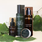 A skincare set from the brands rehua and mareikura skin, including face oil, cleansing serum, body oil, and skin repair balm, styled with green leaves on a light background.
