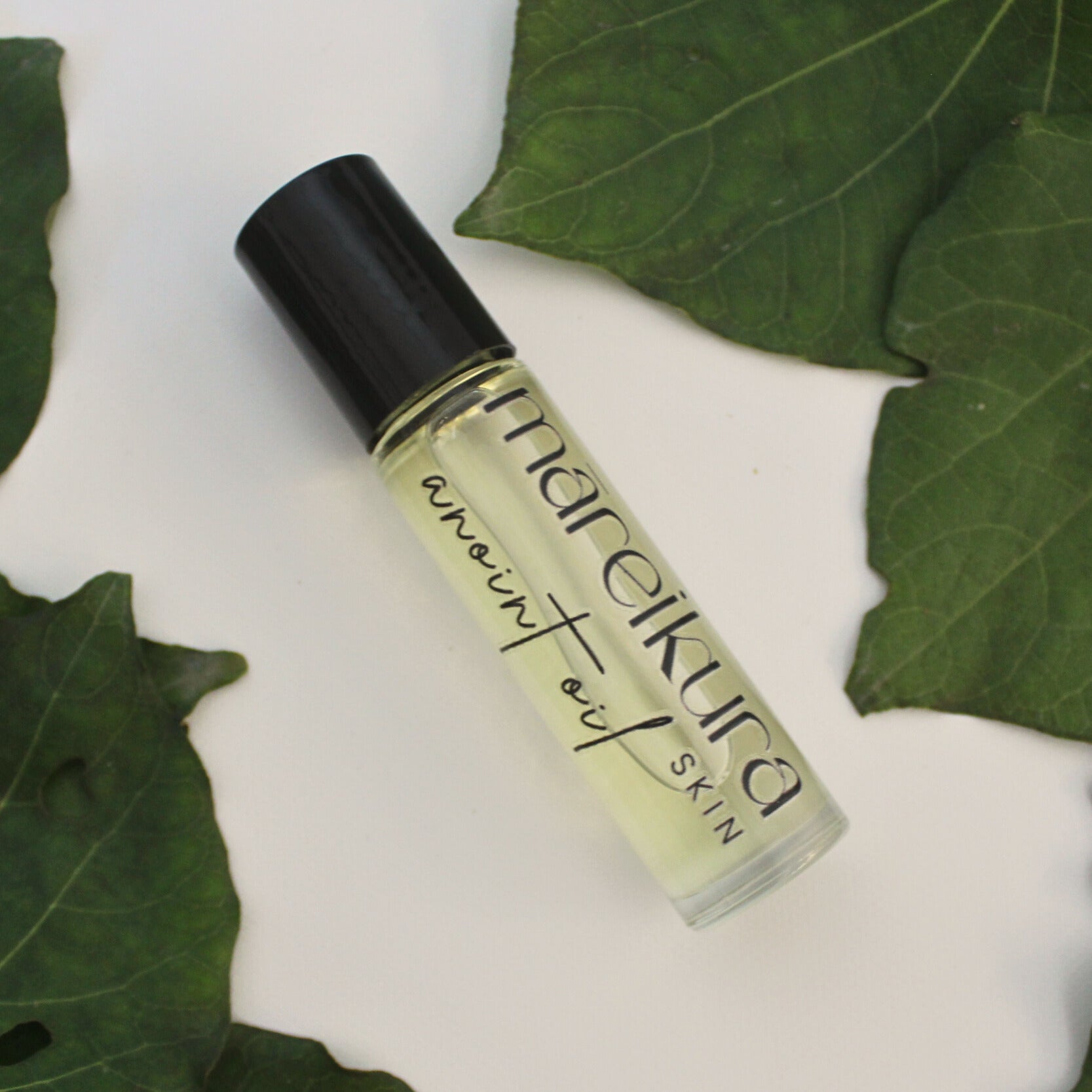 Roll-on bottle of mareikura product on a white background with green leaves