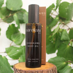 Brown bottle of Māreikura Kawakawa Body Oil on a wooden block with kawakawa leaves in the background