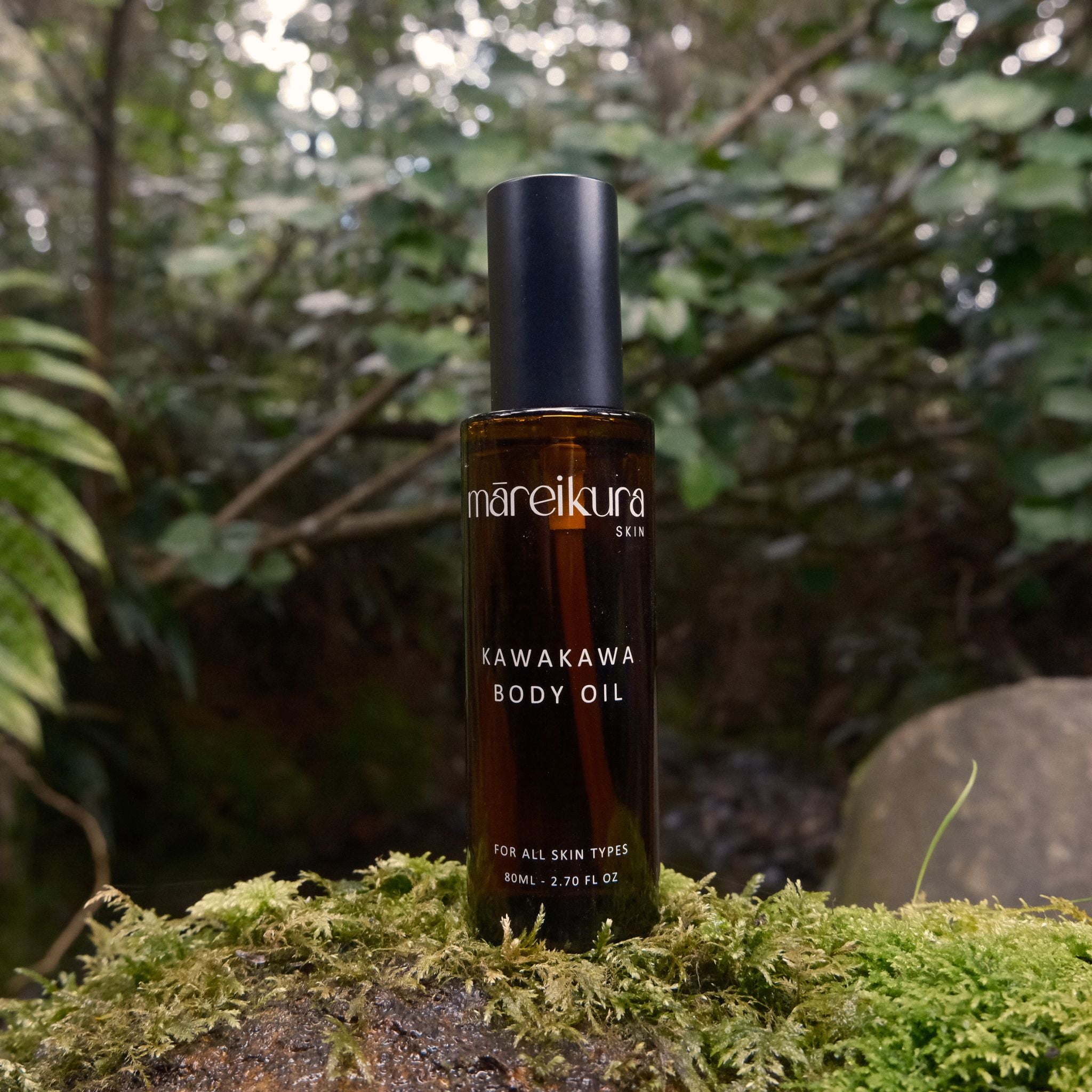 Bottle of mareikura Kawakawa Body Oil on a mossy rock with a forest background