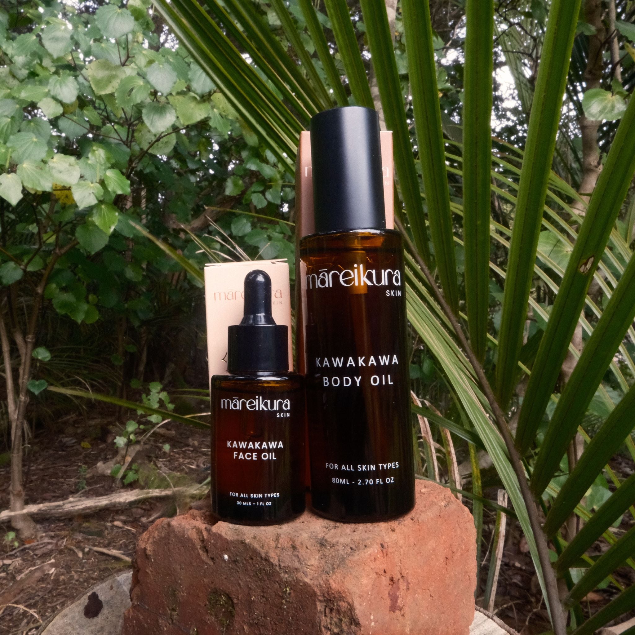Two bottles of Mareikura skincare products on a rock with green foliage in the background