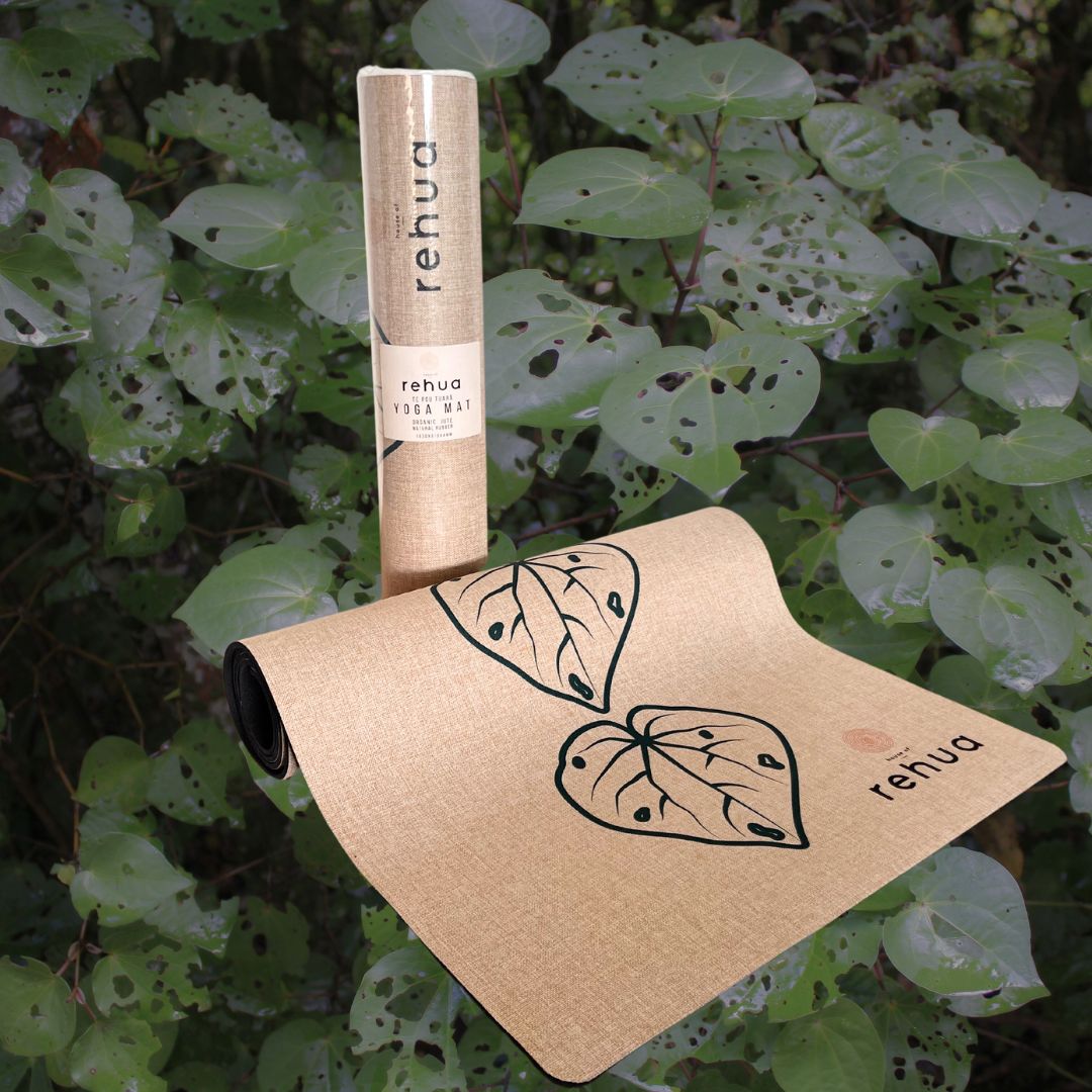yoga mat with rolled-up mat and 'rehua' branding against a green leafy background