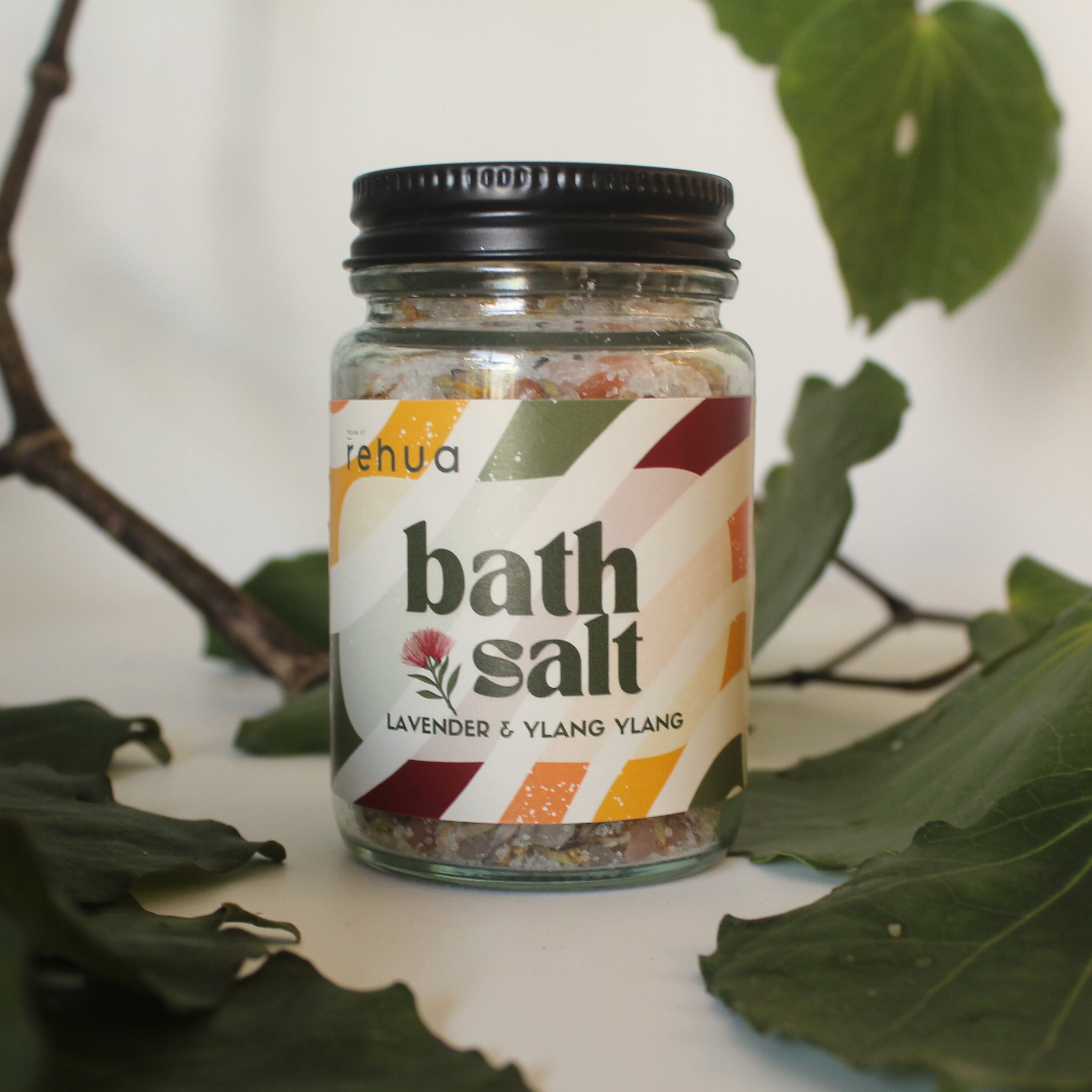 Jar of bath salt with a label on a white surface with green leaves