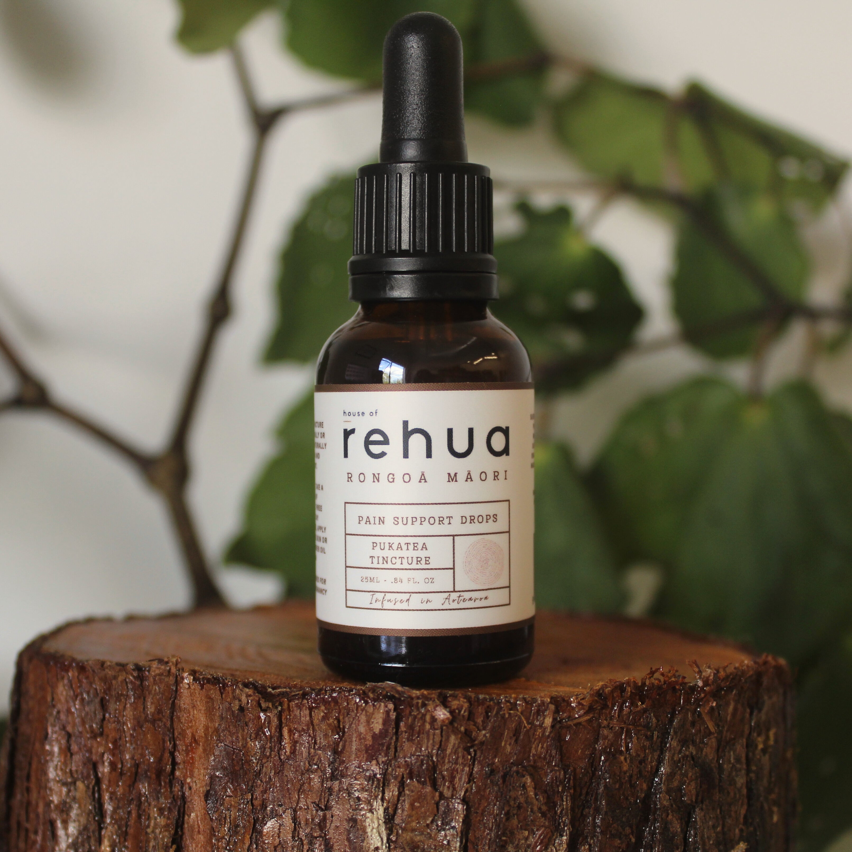 Bottle of Rehua pain support drops on a wooden stump with green leaves in the background