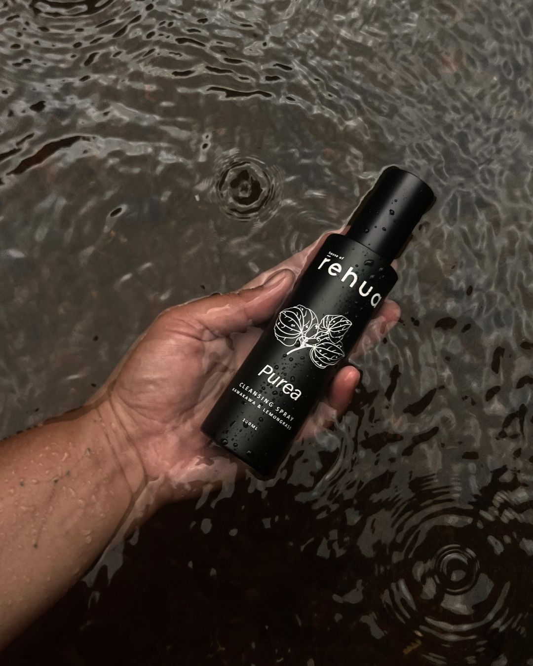 Hand holding a black bottle labeled 'rehuo' over water