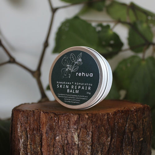 Skin repair balm tin labeled 'rehua' on a wooden stump with green leaves in the background